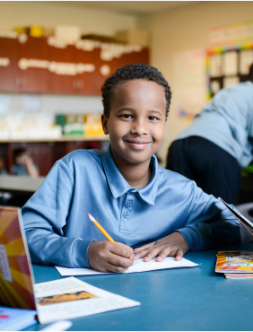 Student boy working at his desk during Opening Ceremony demonstrating focus, responsibility, and readiness to learn.